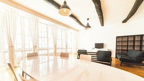 Une salle de conférence avec une grande table, des chaises et un canapé. On y trouve des fenêtres avec des rideaux, un téléviseur et une bibliothèque.