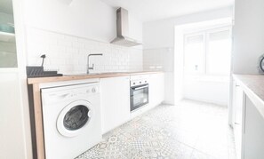 A compact kitchen with a washing machine, oven, and a wooden countertop.