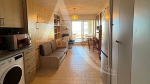 Una cuina compacta amb rentadora, un sofà i una zona de menjador amb taula i cadires.
