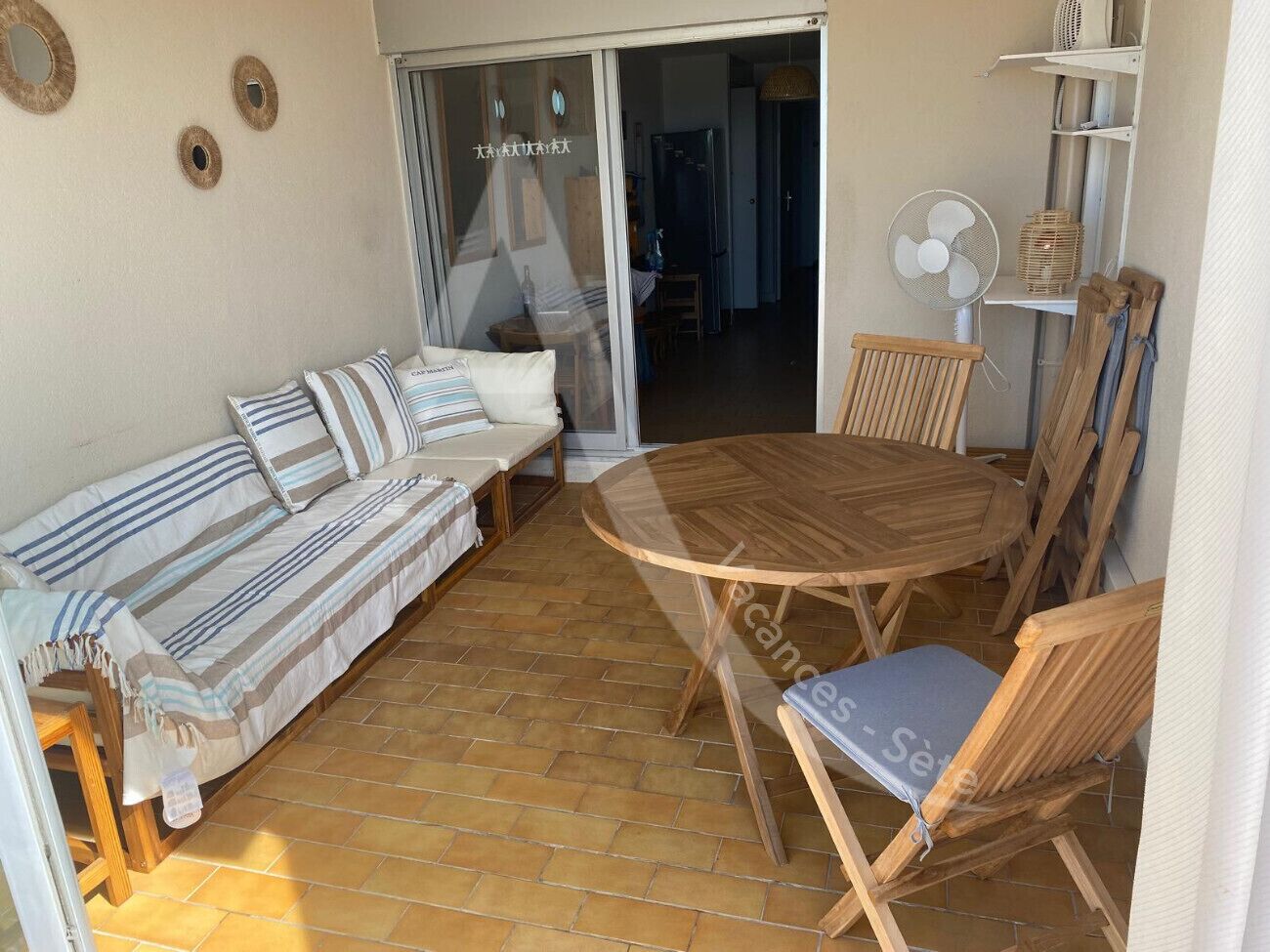 A cozy patio area with a wooden table and chairs, a striped sofa, and a sliding glass door leading to an interior space.