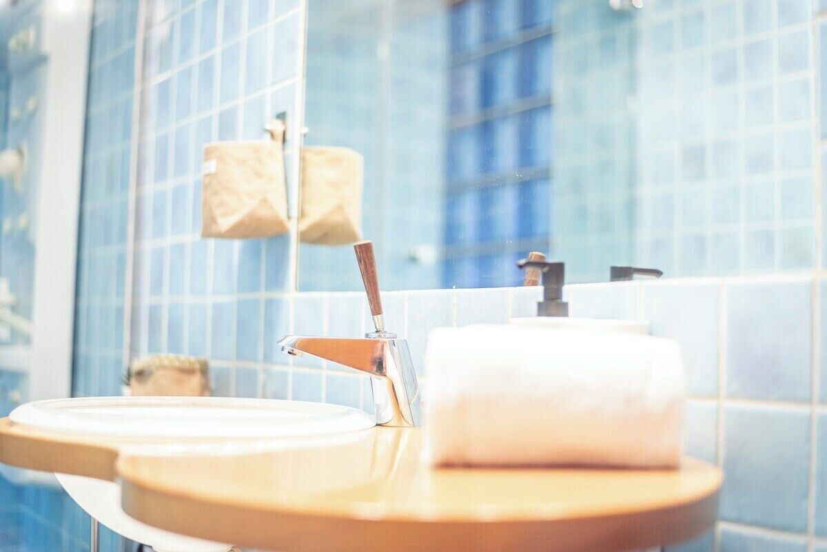 A bathroom with a modern design, featuring a sink with a wooden countertop, a mirror, and a towel dispenser.