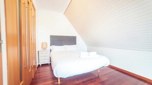 Une chambre avec un plafond en pente, un lit avec une literie blanche, une table de chevet avec une lampe et un plancher en bois.