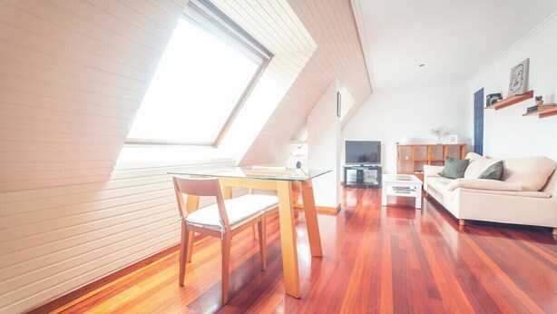 Un salon moderne avec un coin repas, doté d’un plafond en pente, d’un plancher en bois et d’une grande fenêtre qui laisse entrer la lumière naturelle.
