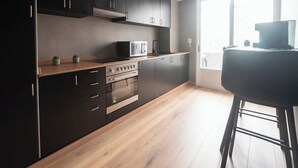 A modern kitchen with dark cabinetry, a microwave, an oven, and a bar stool.