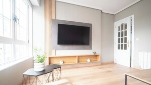 A modern living room with a large TV mounted on the wall, wooden flooring, a small table with a plant, and a door with glass panels.