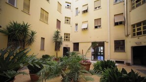 A courtyard with potted plants and a building with multiple windows and balconies. - Chic and Spacious Rome Penthouse (Roma)