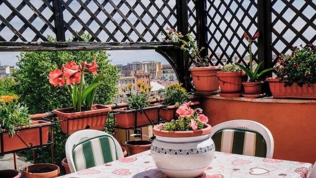 A terrace with potted plants, a table with a heart-patterned tablecloth, and a view of buildings in the background. - Chic and Spacious Rome Penthouse (Roma)