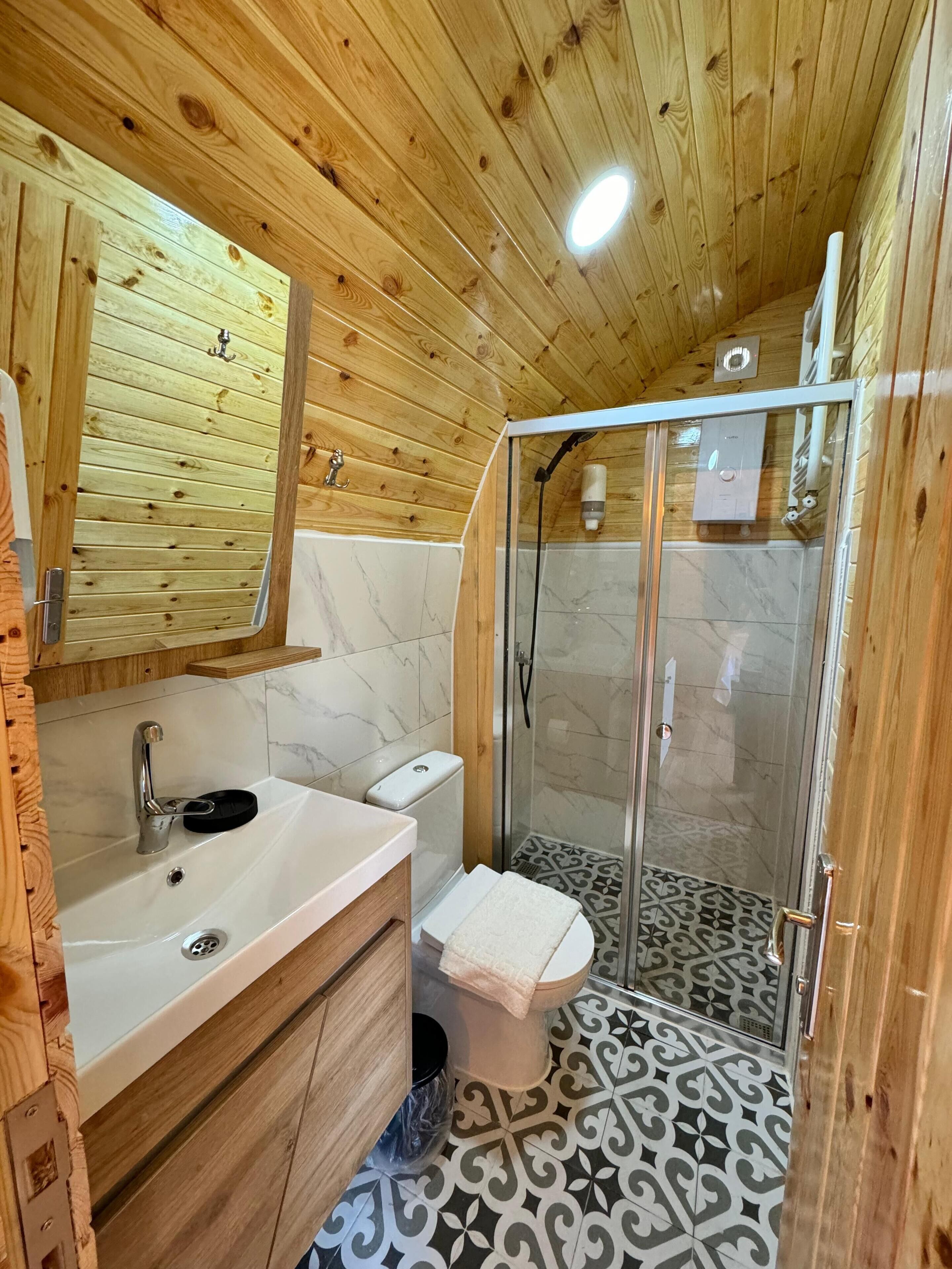 A wooden-paneled bathroom with a sink, mirror, toilet, and shower.
