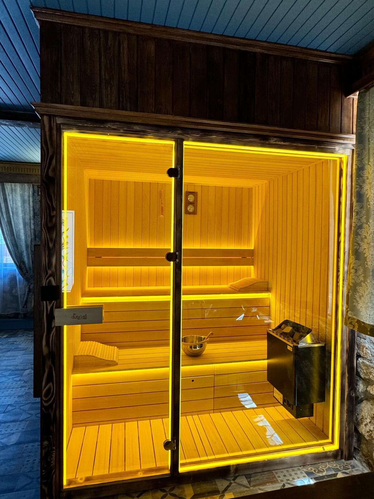 A sauna with wooden walls and a glass door, featuring a small shelf with a towel and a bowl.