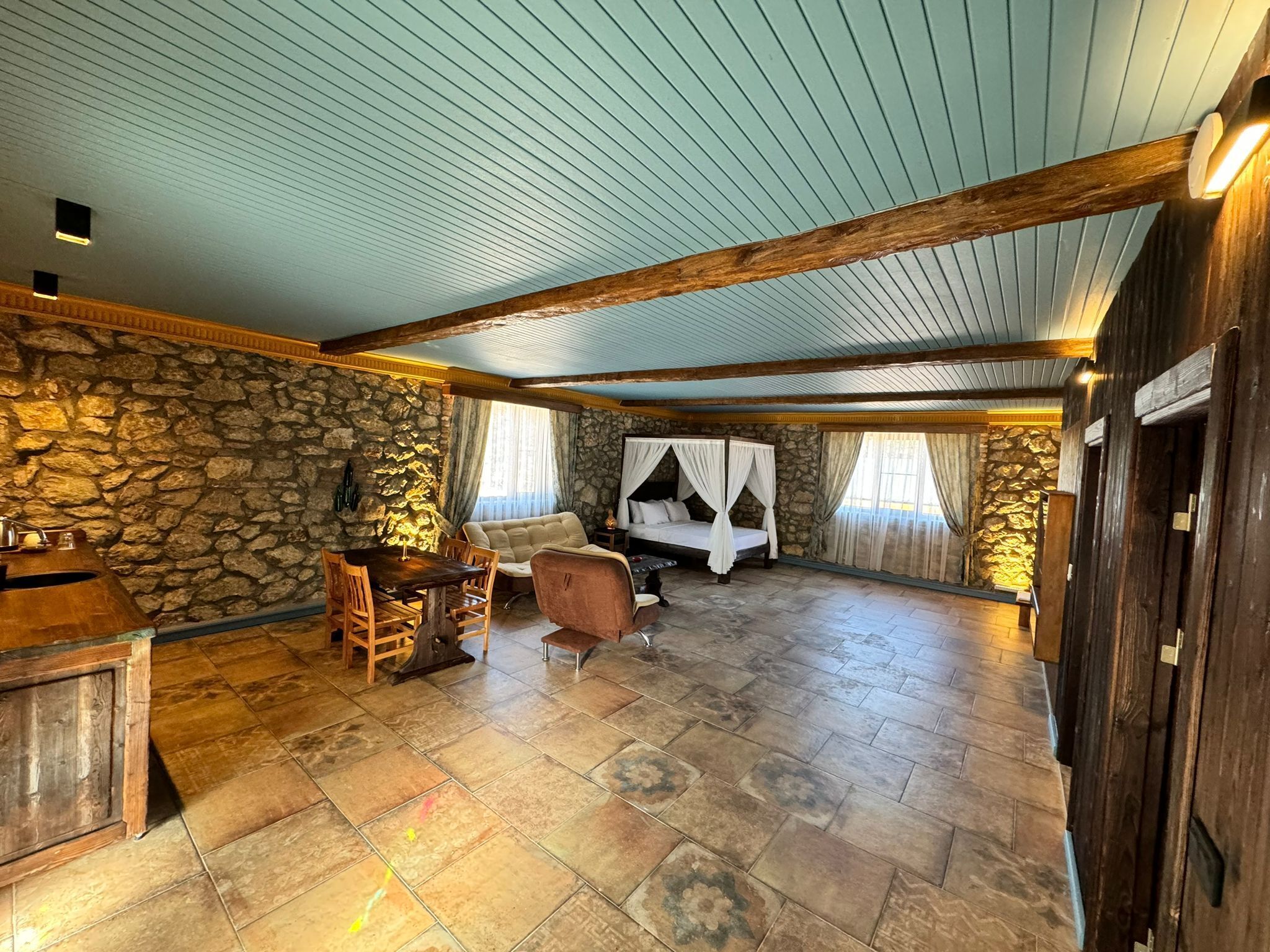 Une pièce spacieuse avec un mur en pierre, une table à manger en bois et un lit à baldaquin.