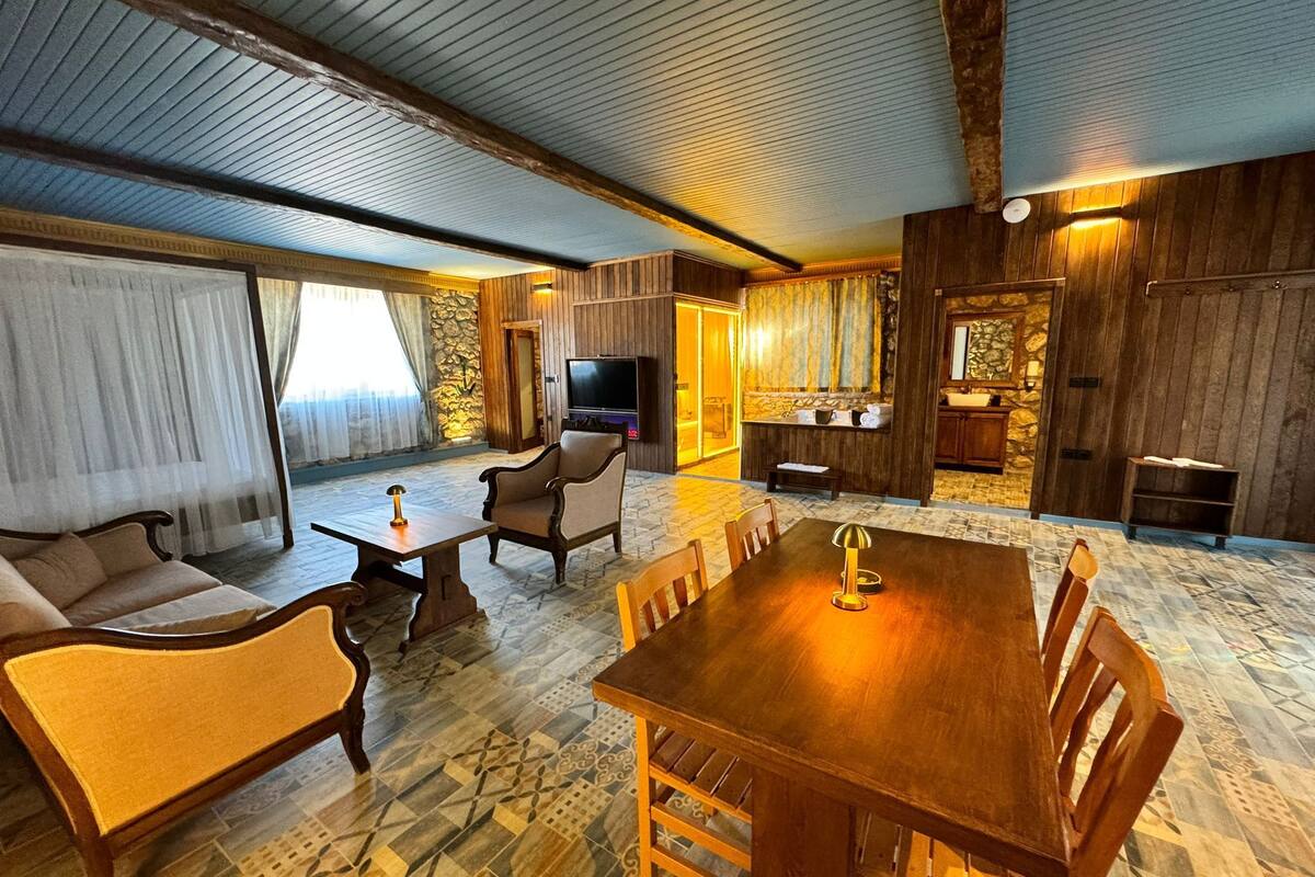 Ein geräumiger Wohnbereich mit einem Holzespeisetisch, bequemen Sitzgelegenheiten, einem Fernseher und einer Wand mit Steinverkleidung.