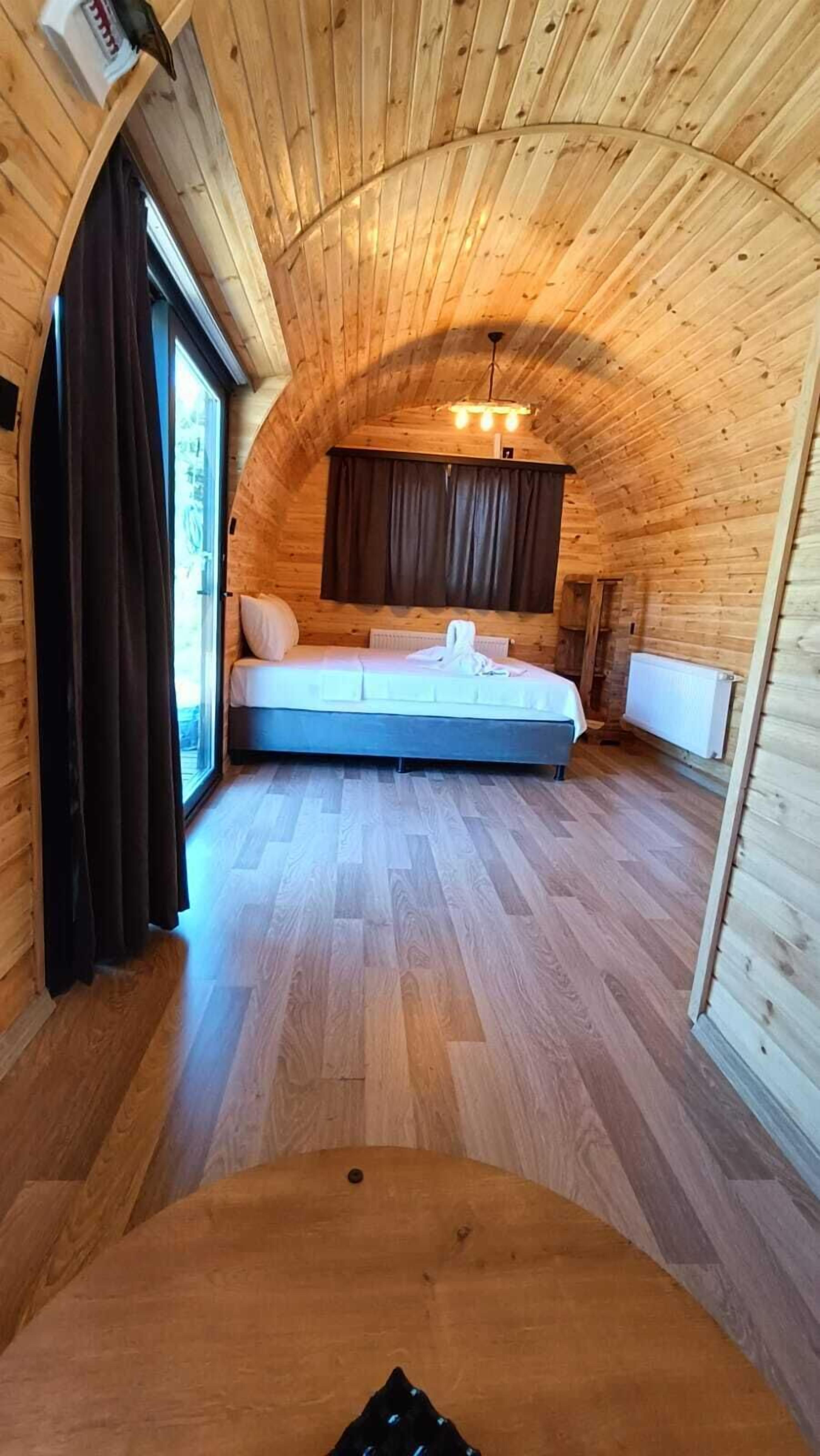 A cozy, wooden cabin bedroom with a bed, a ceiling light, and a window with curtains.