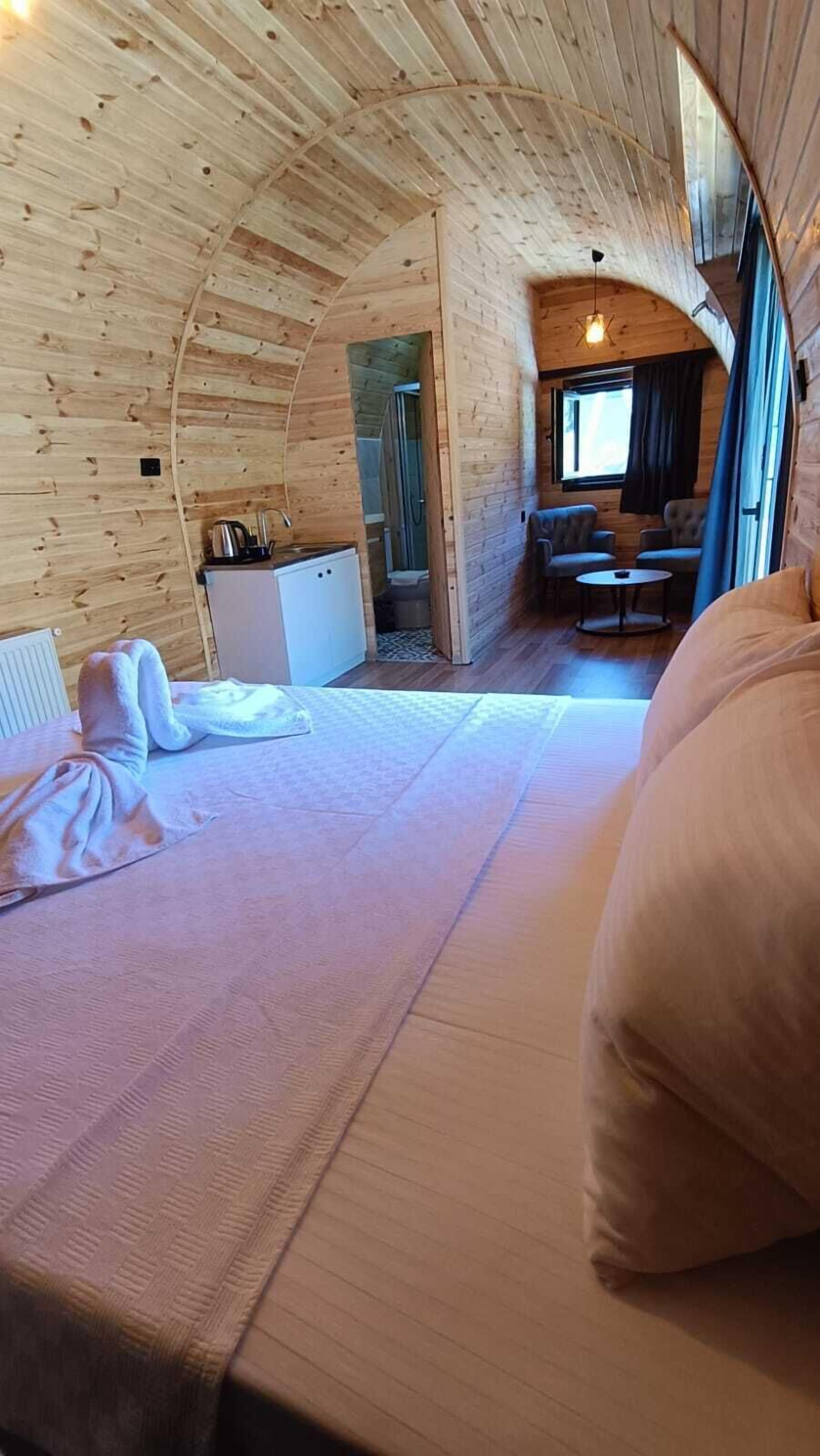 Een gezellig houten kamer met een bed, een kleine kitchenette en een zithoek met uitzicht op de natuur.