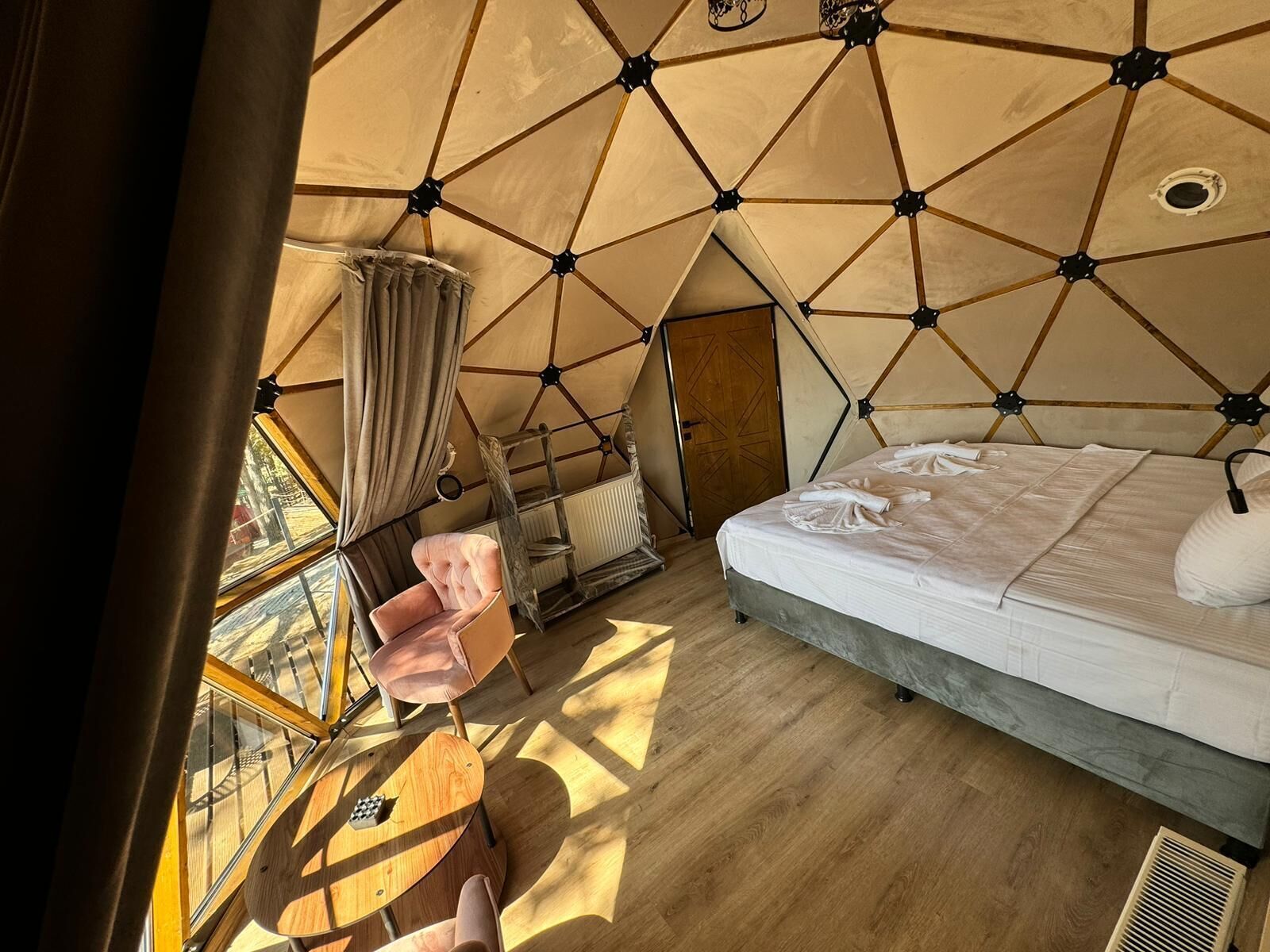Una habitación tipo tienda de campaña, acogedora y triangular, con una cama, una silla y una mesa.