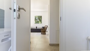 A hallway with a washing machine, a window with a view of trees, a sofa, and a wicker chair.