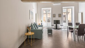 A spacious living area with a sofa, a small table with a plant, a TV, and a dining area with chairs. - MetaM Apartment in the City Center by Wonderful Italy (Palermo)