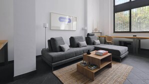 Een moderne woonkamer met een grijze bank, een houten salontafel en een groot raam met uitzicht op bomen.