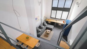 Een moderne woonruimte met een bank, een houten tafel, een klein bijzettafeltje en een groot raam dat voor natuurlijk licht zorgt.