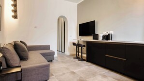 A modern living room with a gray sectional sofa, a flat-screen TV, a coffee machine, and a minimalist kitchen area. - 15min to Duomo, Modern 1 Bedrm Flat A/C, 5G WiFi (Milan)