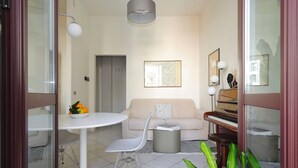A modern living room with a white table, a grey chair, a sofa, a piano, and a potted plant. - Genova25 - One Bedroom Apartment, Sleeps 3 (Milano)