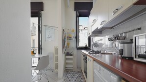 A compact kitchen with a dining area, featuring a modern design with white cabinetry, a tiled backsplash, and a window providing natural light. - Genova25 - One Bedroom Apartment, Sleeps 3 (Milano)
