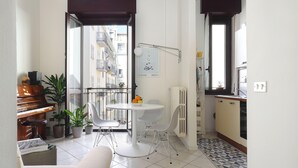 A compact living space with a piano, dining table, chairs, and potted plants. A balcony with a view of buildings is visible through an open door. - Genova25 - One Bedroom Apartment, Sleeps 3 (Milano)