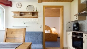 Een kleine keuken met een houten eettafel, een blauwe bank en een bed in de aangrenzende kamer.