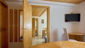 Een slaapkamer met een houten bed, een aan de muur bevestigde televisie en een houten deur met spiegel.