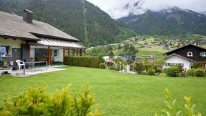 Een huis met een schuin dak, een terras met tafel en stoelen, en een verzorgd gazon.