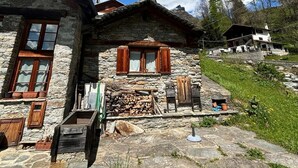 Une maison en pierre avec un porche en bois, une fenêtre avec des volets et une pile de bois de chauffage.