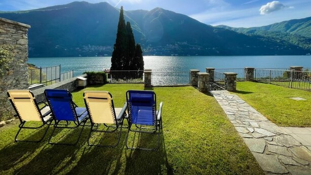 Eine Terrasse mit vier Liegestühlen mit Blick auf einen See und Berge.