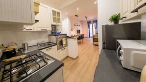A modern kitchen with a gas stove, oven, microwave, and a dining area with a table and chairs. - Chic Modern 2-Bedroom near Metro (Roma)