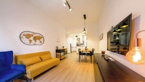 A modern living room with a sofa, a dining table, and a kitchen in the background. - Chic Modern 2-Bedroom near Metro (Roma)