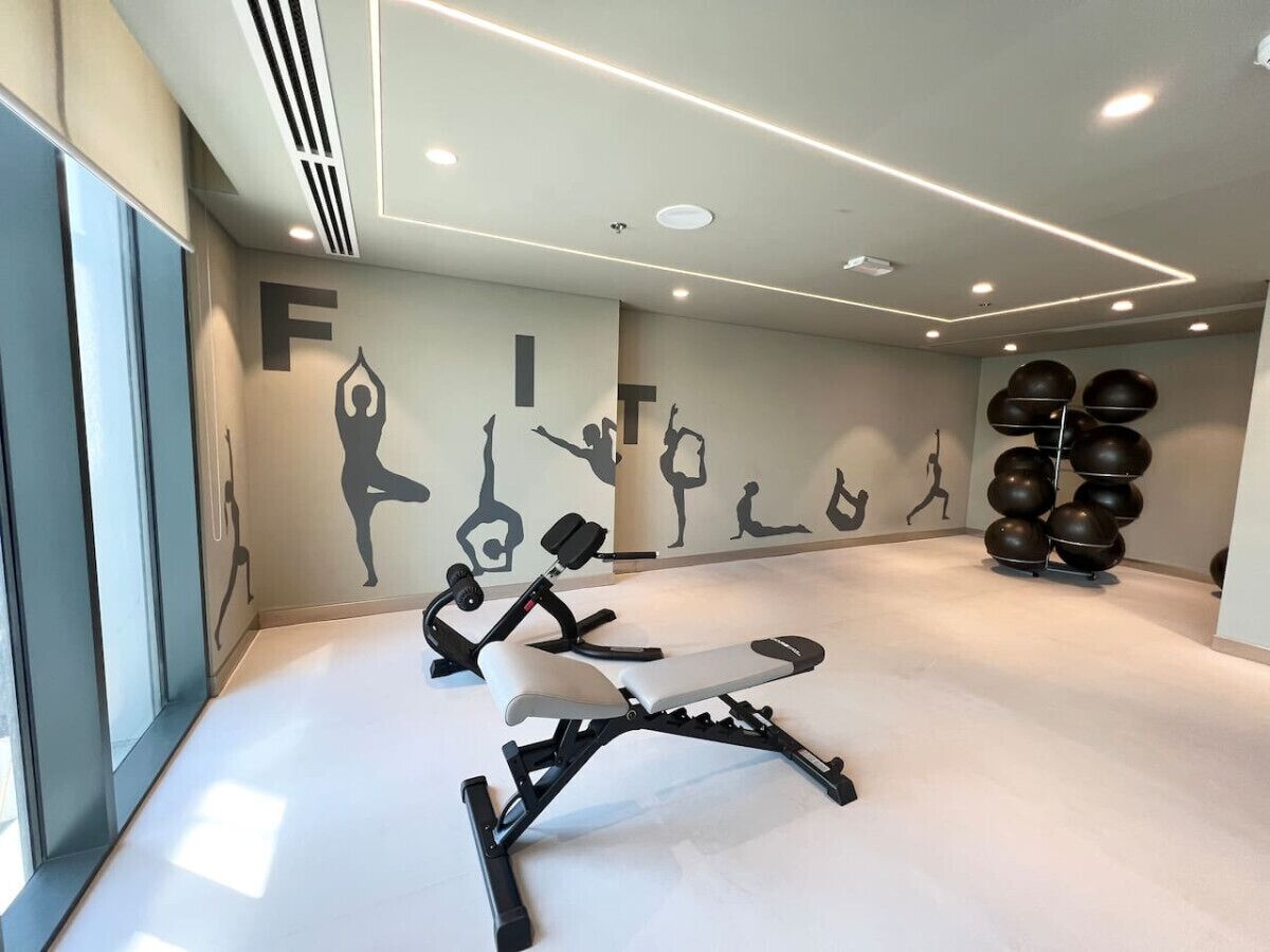 A modern gym with exercise equipment, a wall with fitness silhouettes, and a set of large exercise balls.
