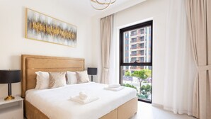 Habitación de hotel con una cama grande, una mesita de noche, una lámpara, una ventana con cortinas y vistas a la ciudad.