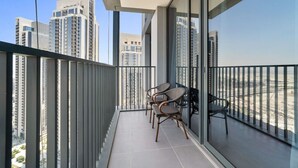 A balcony with a view of high-rise buildings, a glass partition, and two wicker chairs.