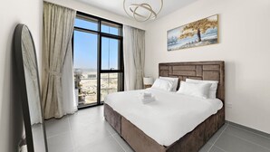 A hotel room with a large bed, a view of the city, and a painting on the wall.