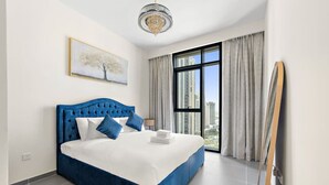 Ein modernes Schlafzimmer mit einem großen Bett, einer Chandelier, Blick auf die Stadt und einem Gemälde an der Wand.