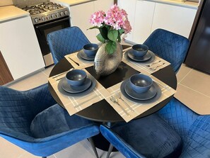 Ein Esstisch mit blauen Stühlen, eine Vase mit rosa Blumen und ein moderner Herd im Hintergrund.