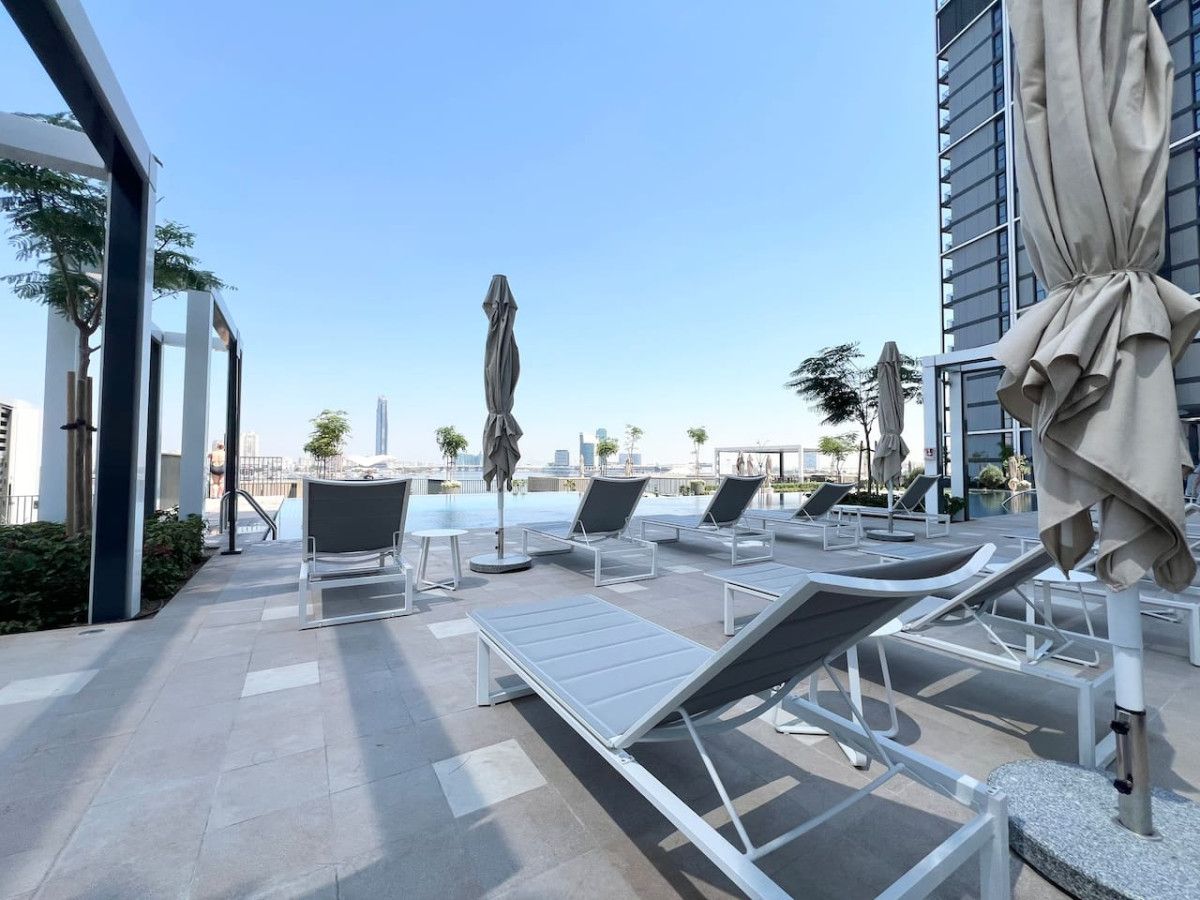 A rooftop pool area with sun loungers and umbrellas, overlooking a cityscape.