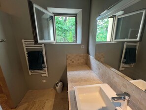 Une salle de bain avec une baignoire, une fenêtre, un porte-serviettes et une poubelle.