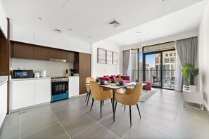 A modern kitchen with a dining area, a balcony with a city view, and a living space with a sofa and chairs.