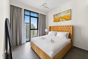 A hotel room with a large bed, a city view, and a painting on the wall.