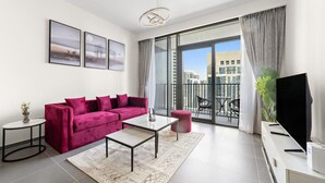 A modern living room with a red sofa, a coffee table, and a TV on a stand. There are two framed pictures on the wall, a small side table, and a balcony with a view of buildings. - HomesVIP | High-Class | Brand New (Dubai)