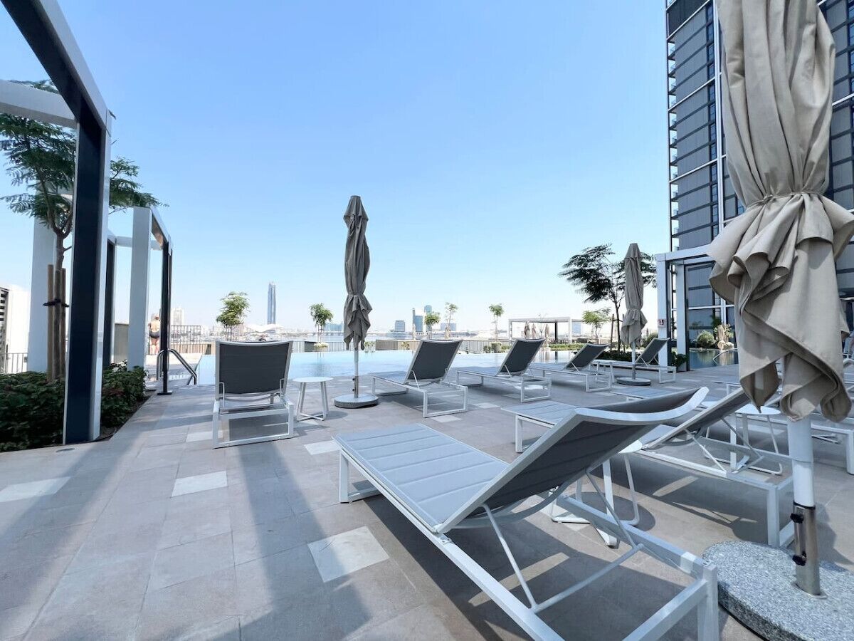 Uma área de piscina no terraço com espreguiçadeiras e guarda-sóis, com vista para a paisagem urbana.