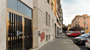 En smal gade i byen med parkerede biler og en bygning med tremmevinduer og graffiti.