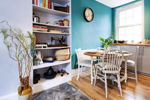 A room with a teal wall, a white bookshelf, a dining table with chairs, and a window with a view. - Lovely Portobello Apartment near Westbourne Park (London)