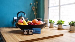 Una mesa de madera con un cuenco de frutas, frascos y un hervidor.