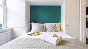 Un dormitorio ordenado con una pared de acento color turquesa, un edredón acolchado y una toalla doblada sobre la cama.