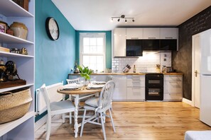 A modern kitchen with white cabinets, a wooden dining table, and a blue accent wall. - Lovely Portobello Apartment near Westbourne Park (London)